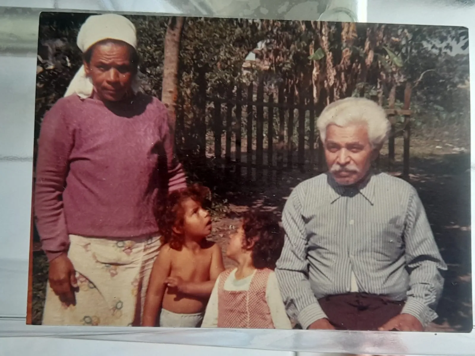 Foto de Mariazinha com seus dois filhos e seu companheiro em frente à uma cerca de madeira.
